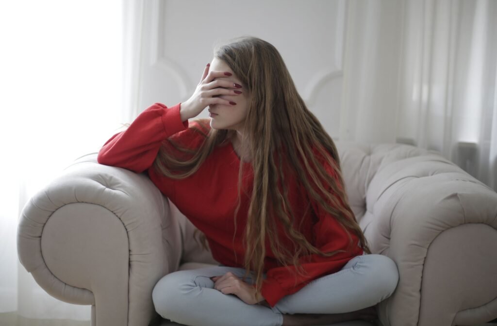 Woman with long hair sits on an armchair, dressed in a red sweater indoors.